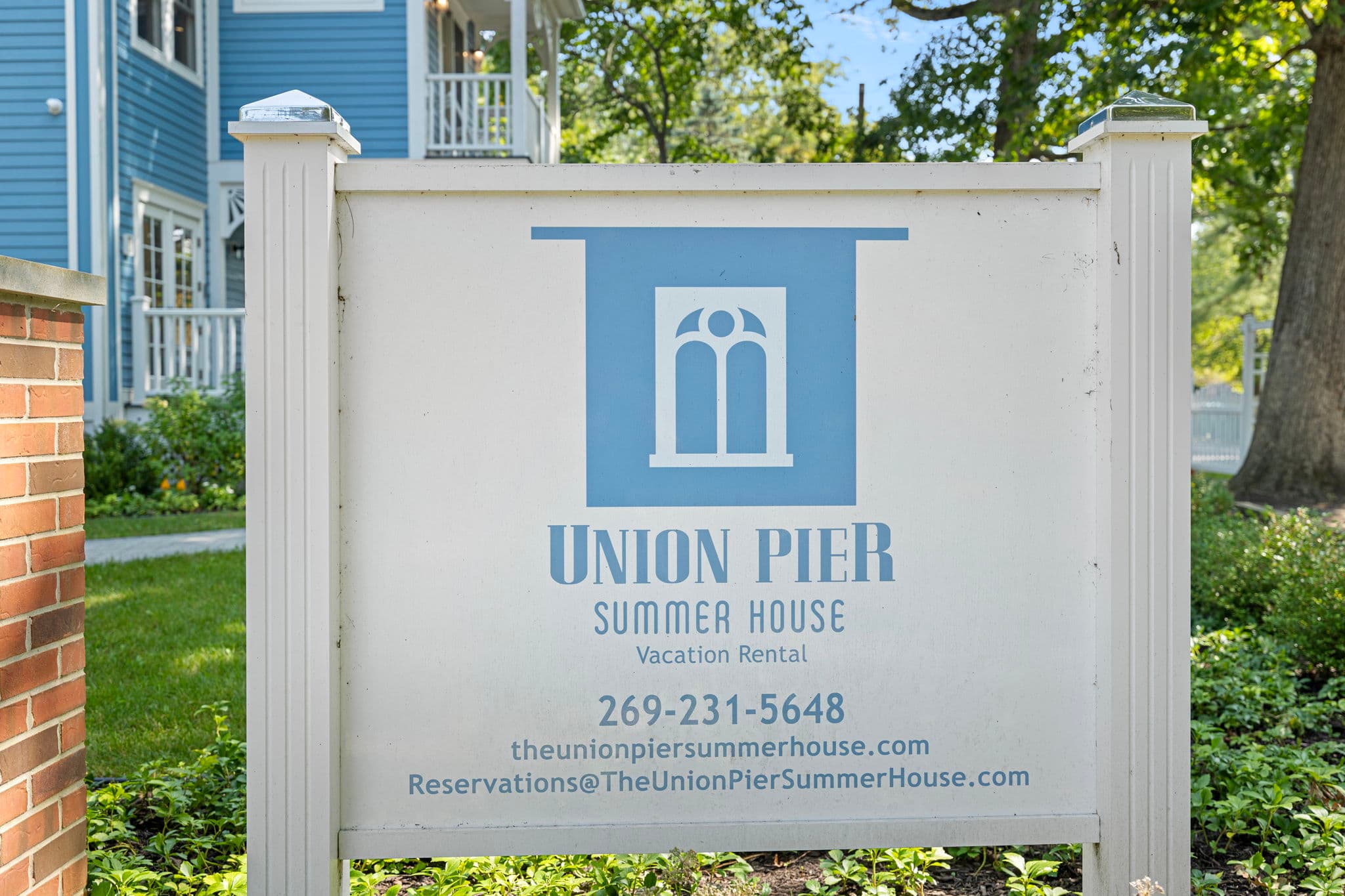 A close-up shot of a white rectangular sign for "Union Pier Summer House" featuring a blue logo of a house.