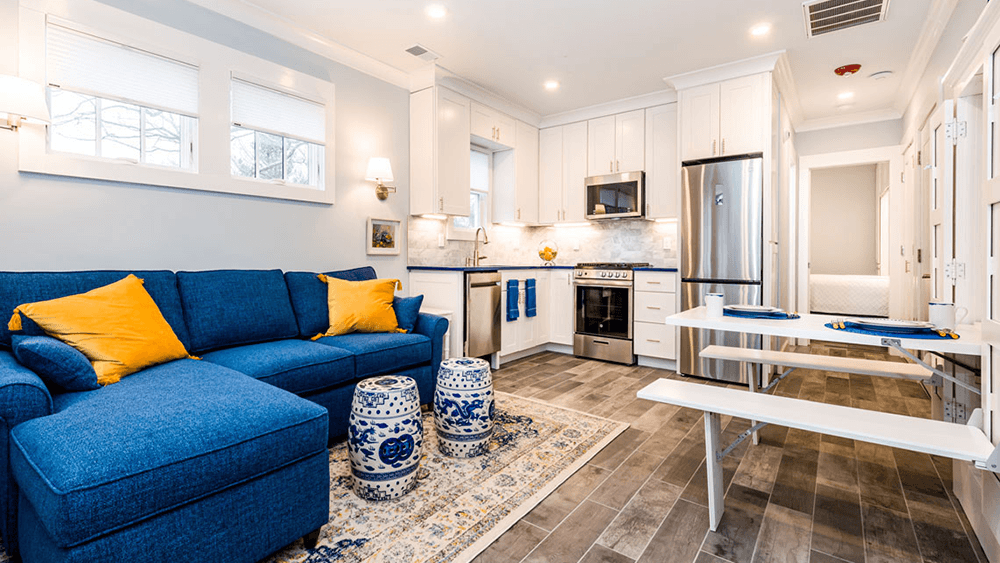 Cozy living area with a blue sectional sofa, decorative stools, and modern kitchen appliances.
