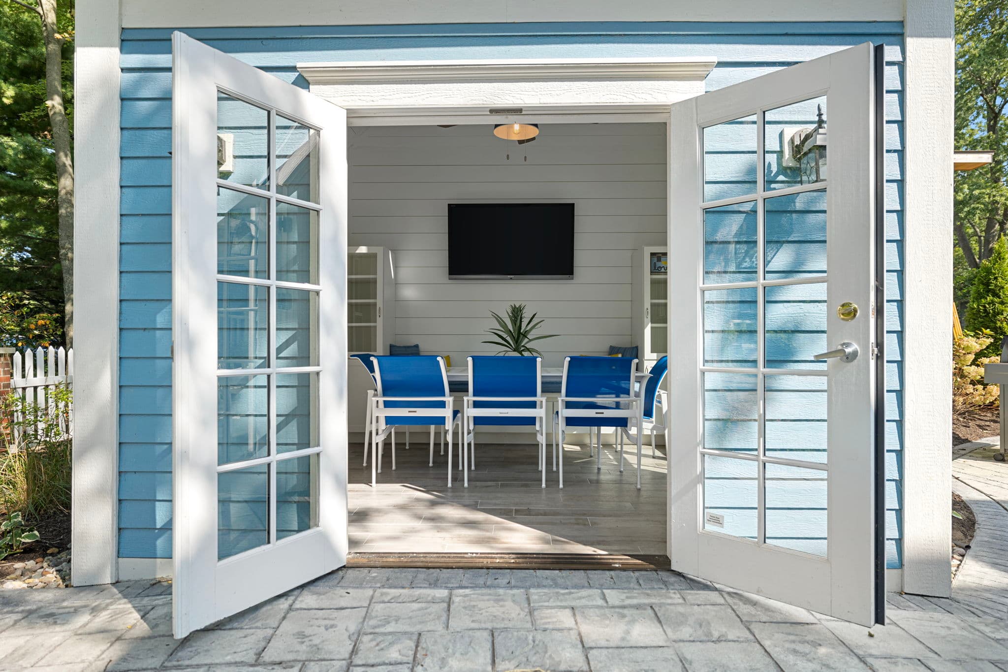 Open double doors reveal a stylish, light-filled patio with a dining area and a television.