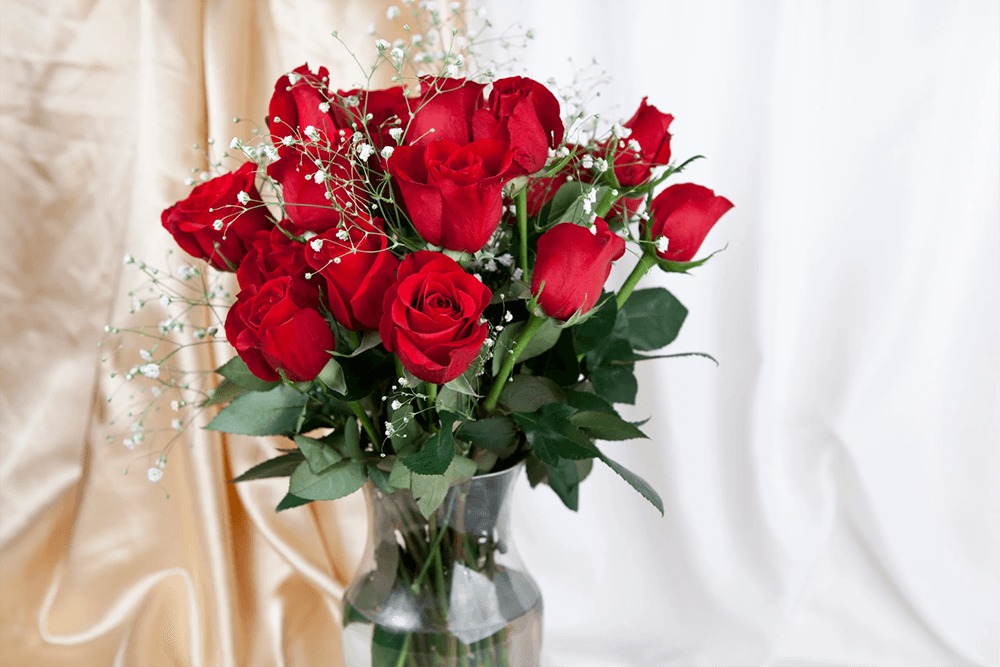 A bouquet of vibrant red roses with baby's breath in a clear vase.