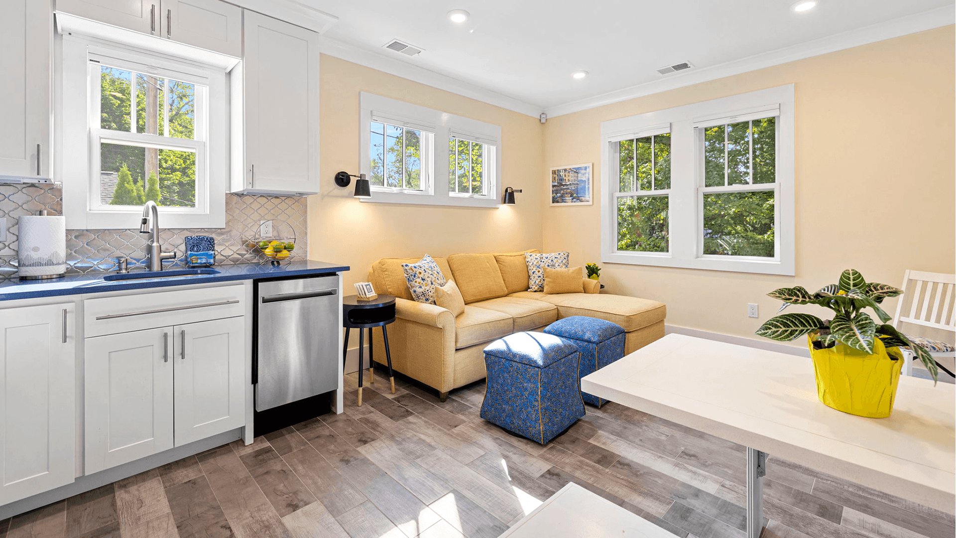 Bright and modern living room with a yellow sofa, blue accent pieces, and a kitchenette.