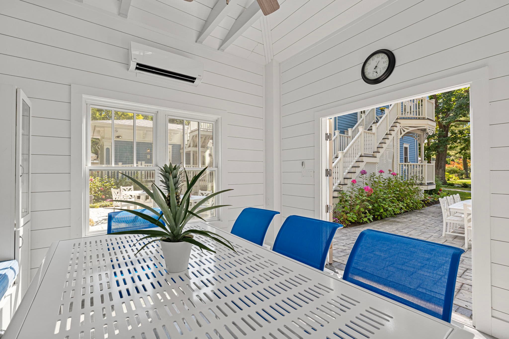 Bright dining area with a white table, blue chairs, and a view of an outdoor patio and garden.